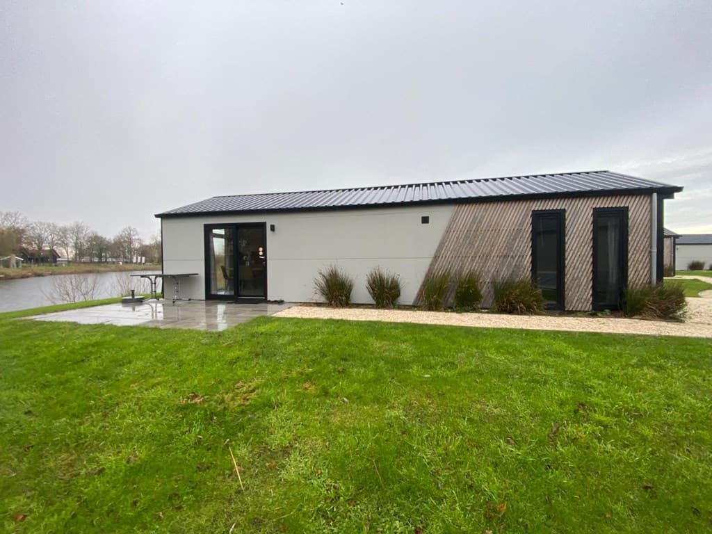 Moderne woning aan het water met een grasveld en bestrating, grote ramen en houten gevelbekleding.