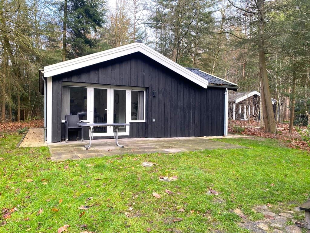 Zwart houten vakantiehuis omringd door bomen met een terras en grote glazen deuren naar de tuin