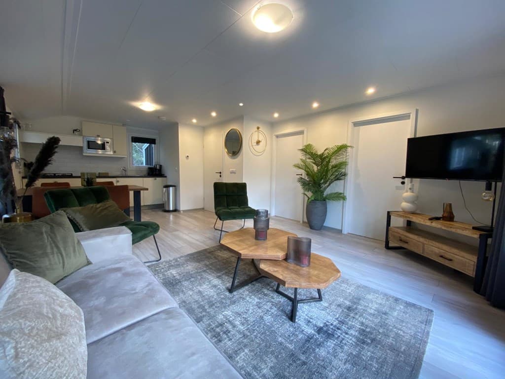 Woonkamer met een stijlvolle inrichting, groene stoelen, een houten salontafel en een moderne televisie tegen de muur.