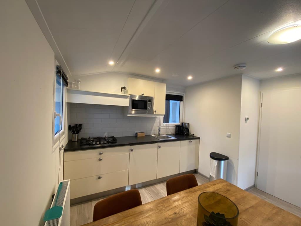 Moderne keuken met witmeubel en zwart aanrecht, tafel met stoelen, en apparatuur zoals een oven en kookplaat