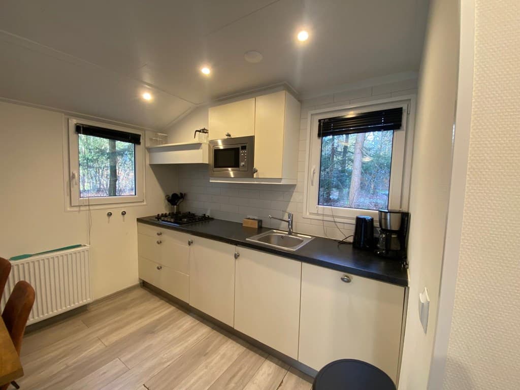 Moderne keuken met witte kastjes, een aanrecht, een oven en ramen met uitzicht op de bomen.