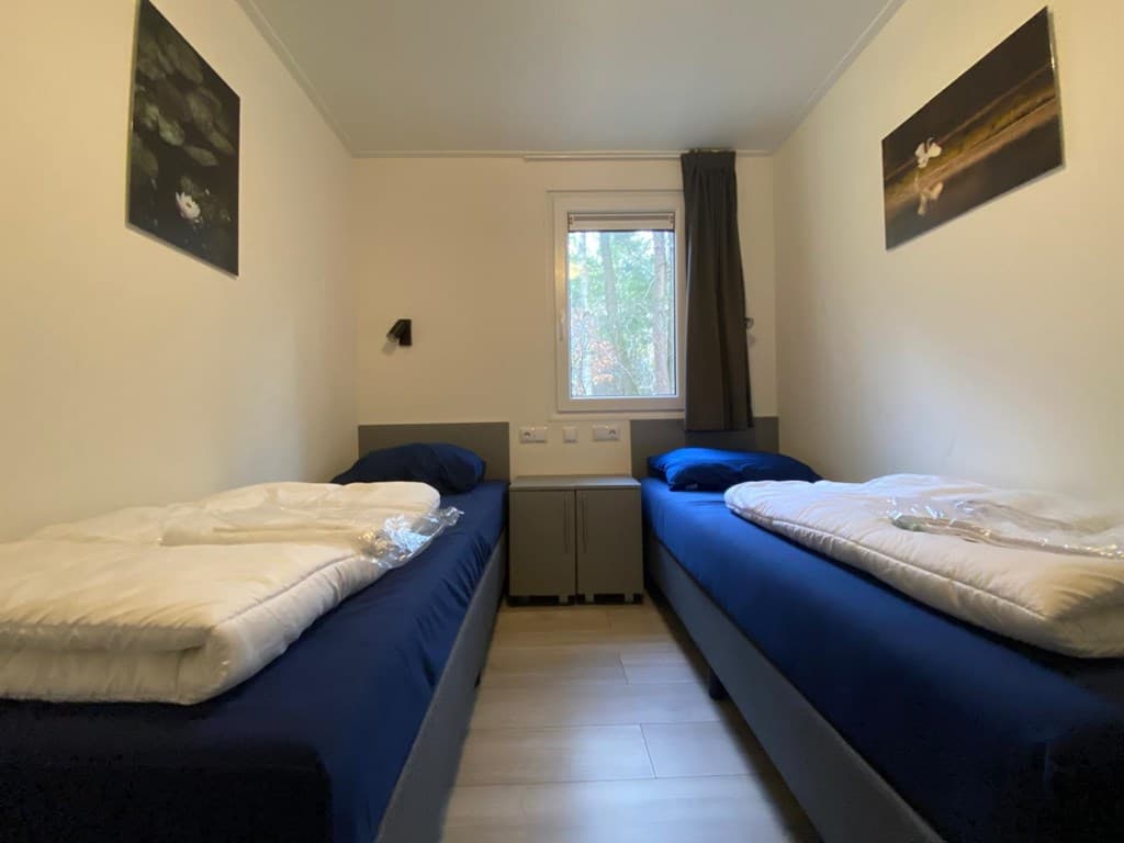 Slaapkamer met twee eenpersoonsbedden, raam met uitzicht op bomen en twee schilderijen aan de muur