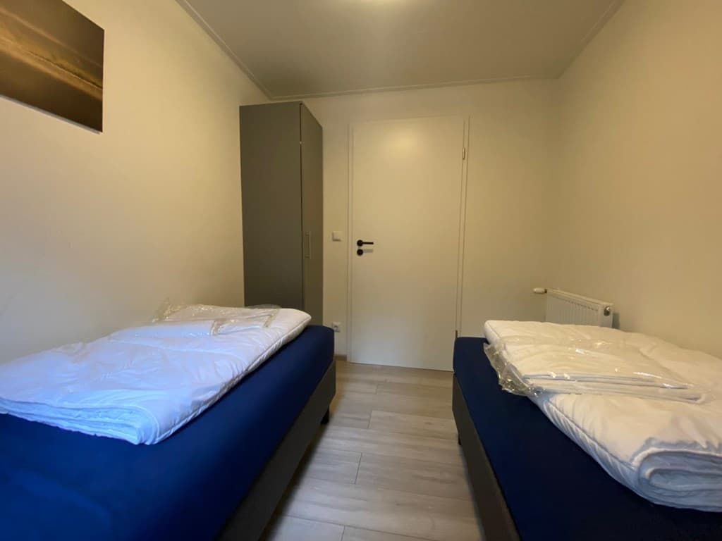 Sfeervolle slaapkamer met twee eenpersoonsbedden, kastruimte en een deur naar een gang.