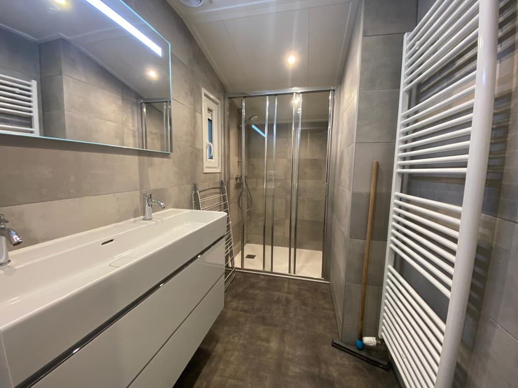 Moderne badkamer met inloopdouche, dubbele wastafel en handdoekradiator in neutrale kleuren