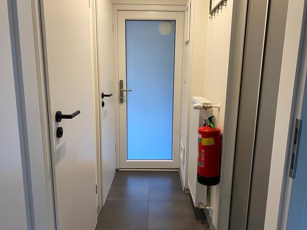 Ingang van de woning met een lange gang, een deur naar buiten en een rode brandblusser aan de muur