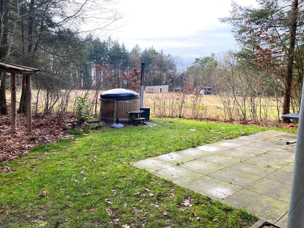Tuin met gras en sierbestrating, houtgestookte hot tub en bomen op de achtergrond met open veld.