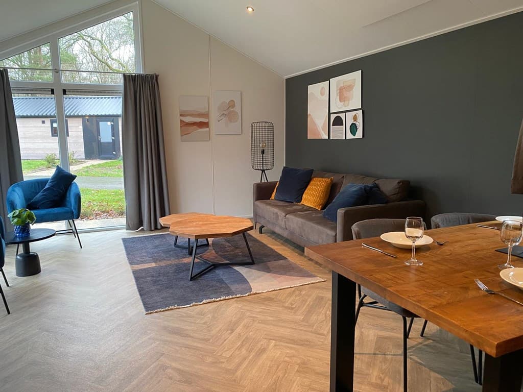 Moderne woonkamer met een zithoek, een houten tafel en grote ramen met uitzicht op het groen.