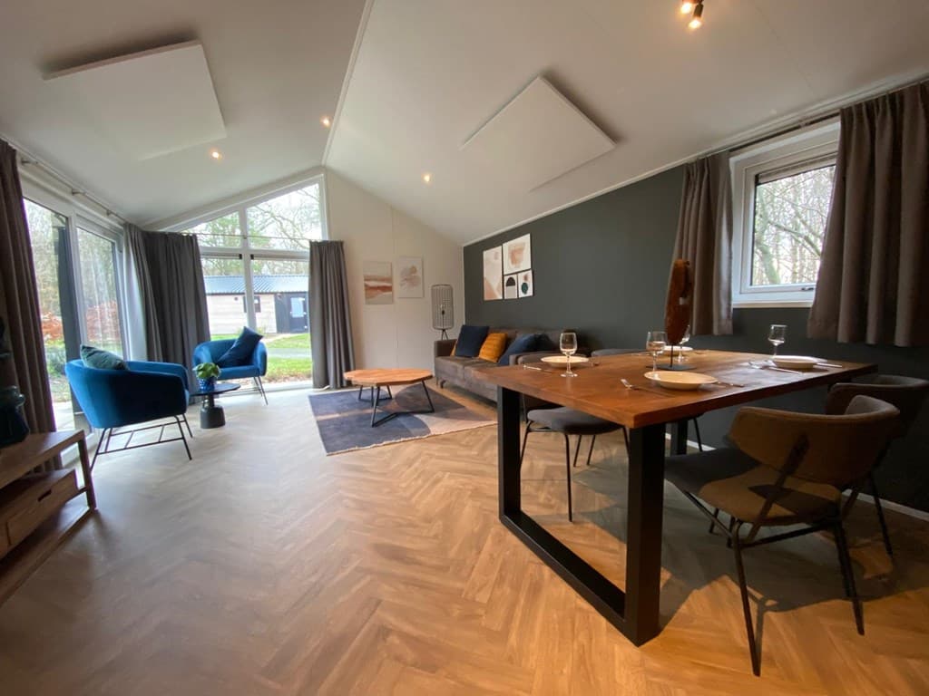 Ruime woonkamer met grote ramen, eettafel, comfortabele stoelen en uitzicht op de buitenruimte van de woning
