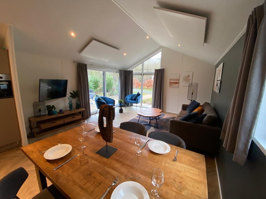 Lichte woonkamer met moderne meubels, eettafel, zithoek en grote ramen met uitzicht op de tuin.