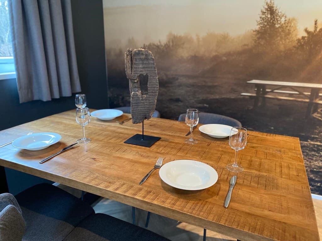 Eettafel met vier borden en glazen, decoratief object in het midden, op een donkere achtergrond met natuurprint.