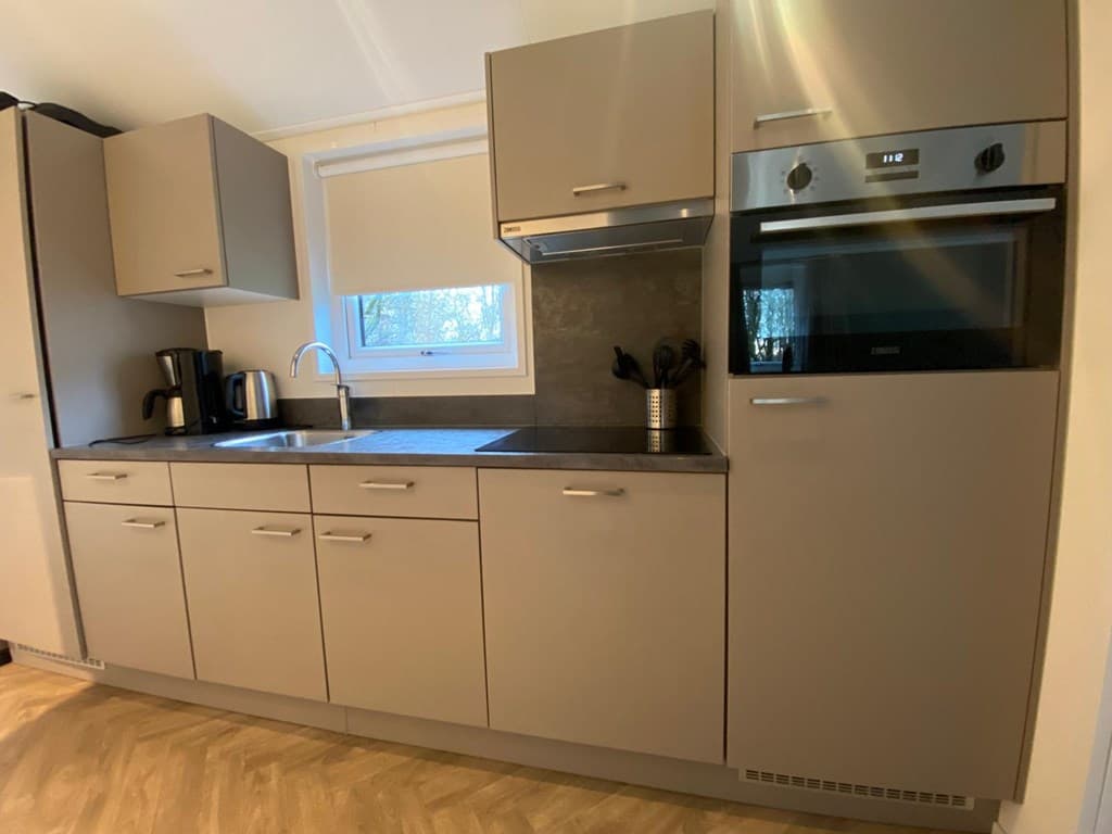 Moderne keuken met grijze kasten, aanrecht, wasbak en ingebouwde oven boven de koelkast.