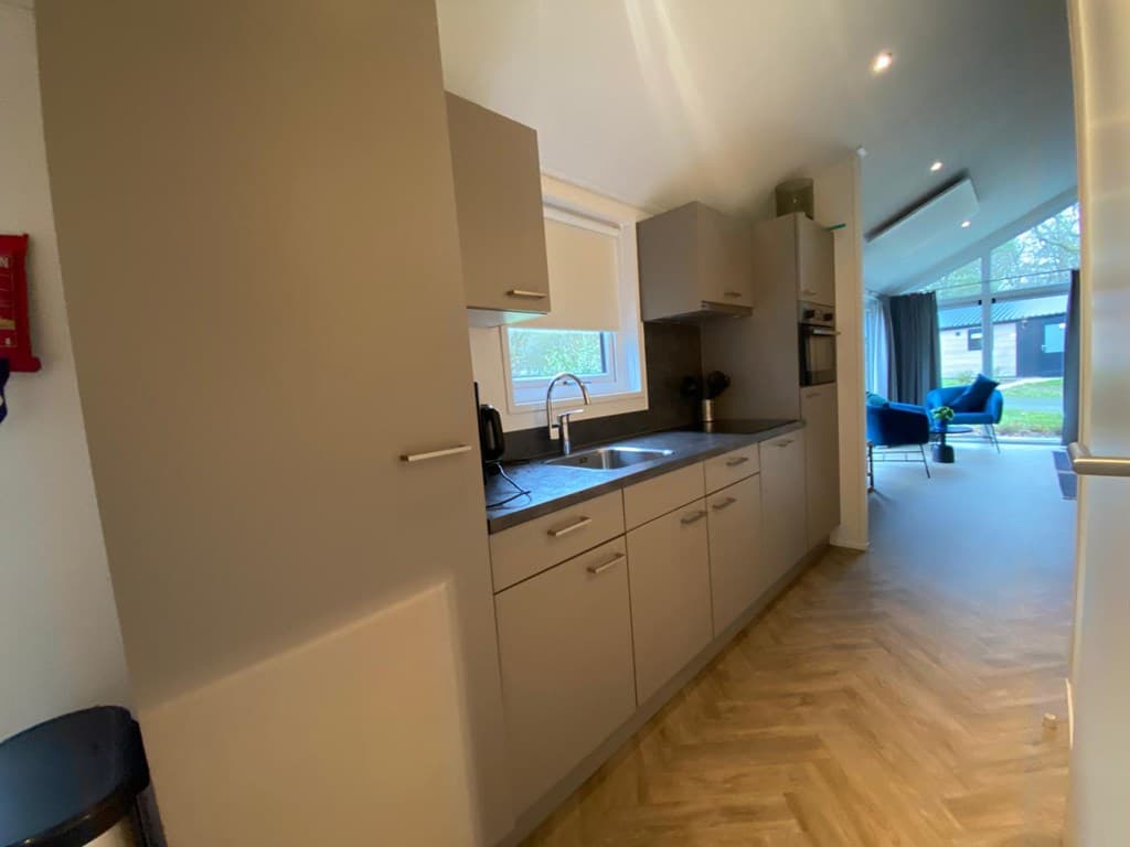 Moderne keuken met inbouwkasten, spoelbak en apparatuur, met uitzicht op de woonkamer en natuurlijke verlichting.