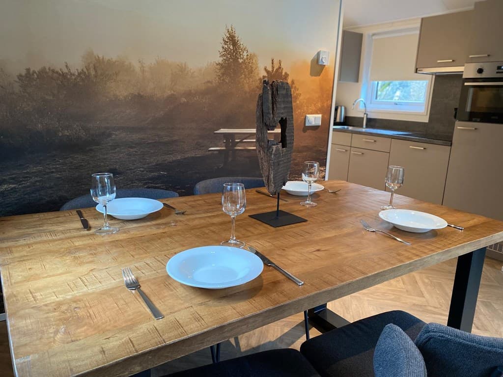 Eetkamertafel met vier borden en glazen, op de achtergrond een natuurwanddecoratie en een moderne keuken.