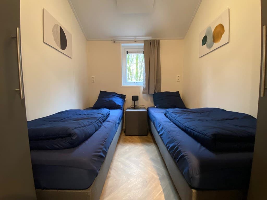 Slaapkamer met twee eenpersoonsbedden, nachtkastje en raam met uitzicht op bomen.