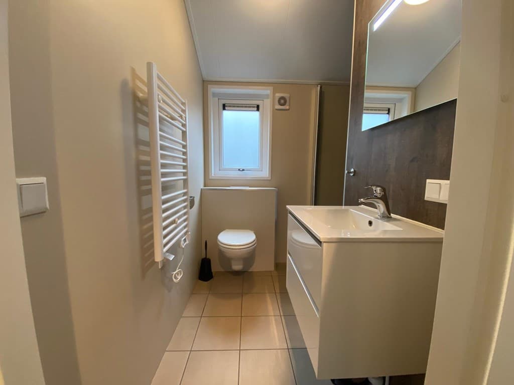 Badkamer met naar voren gericht toilet, wastafel met spiegel en douchecabine, rustige kleuren en vloertegels