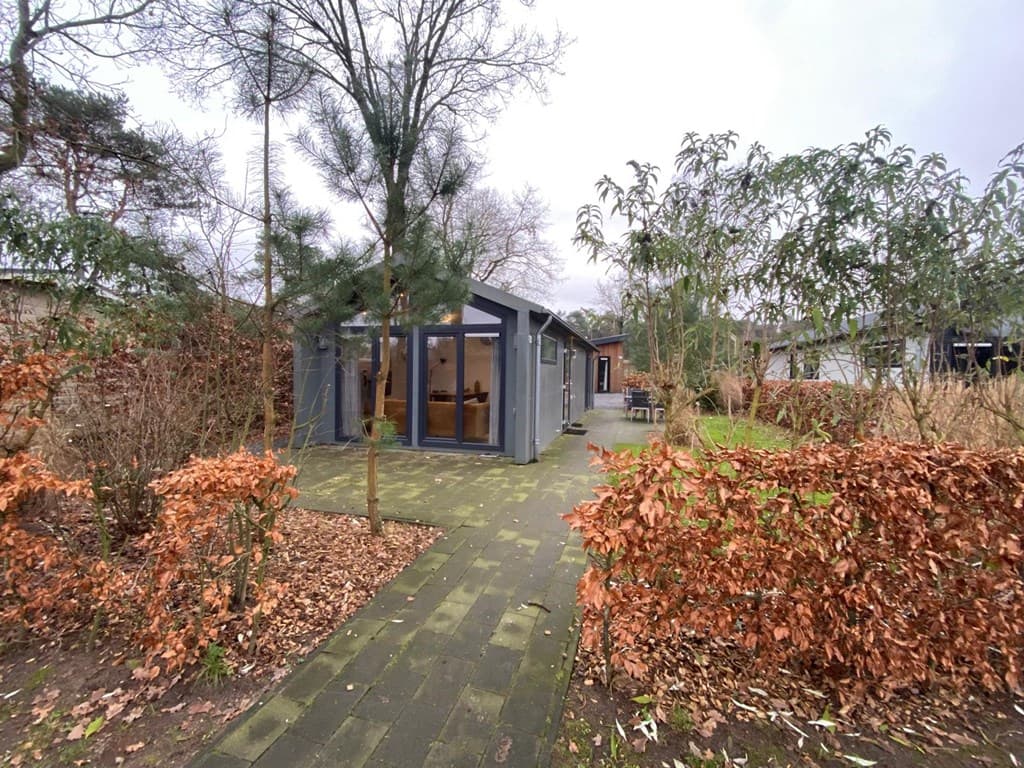 Moderne vakantiewoning omringd door groen en hagen, met een betegeld pad naar de ingang