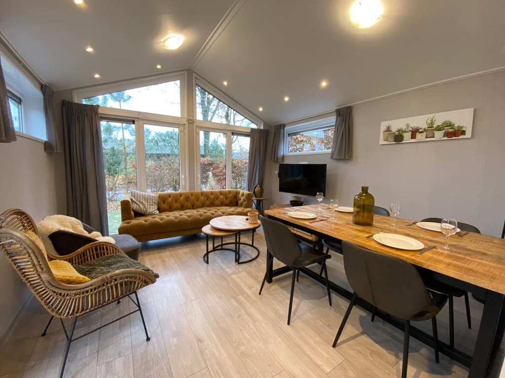 Gezellige woonkamer met grote ramen, een comfortabele bank, eettafel en stijlvol ingericht met planten en decoratie