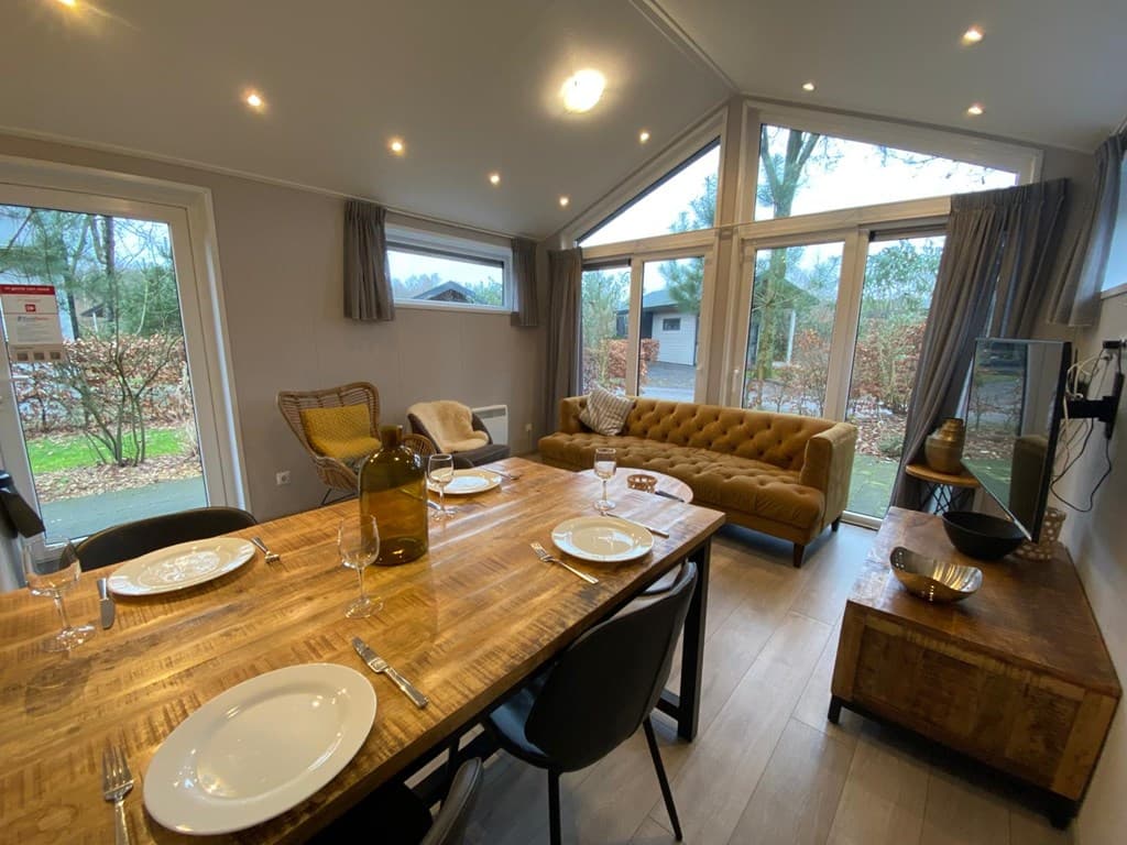 Binnenzicht van een gezellige eetkamer met een houten tafel, stoel en bank, grote ramen met uitzicht op de tuin