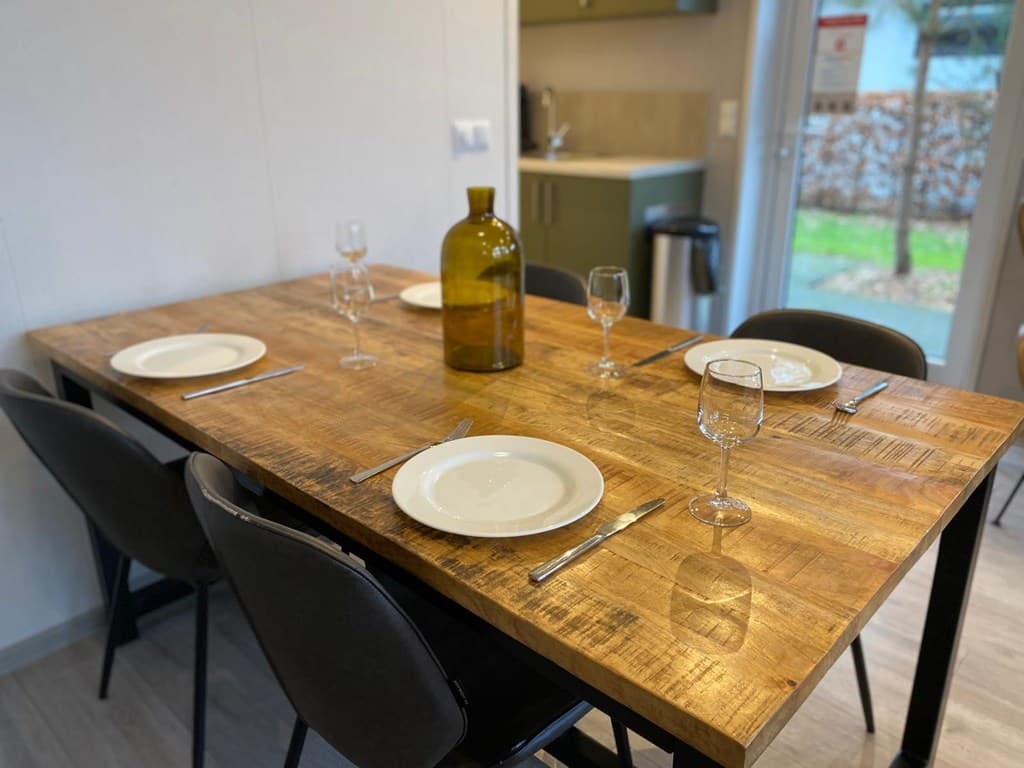 Eettafel met vier borden, glazen en een grote fles, in een lichte woning met zicht op de tuin.
