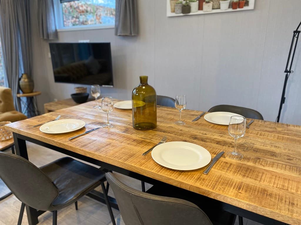 Eettafel met vier borden, glazen en een grote fles in een gezellige woonkamer met televisie en zithoek