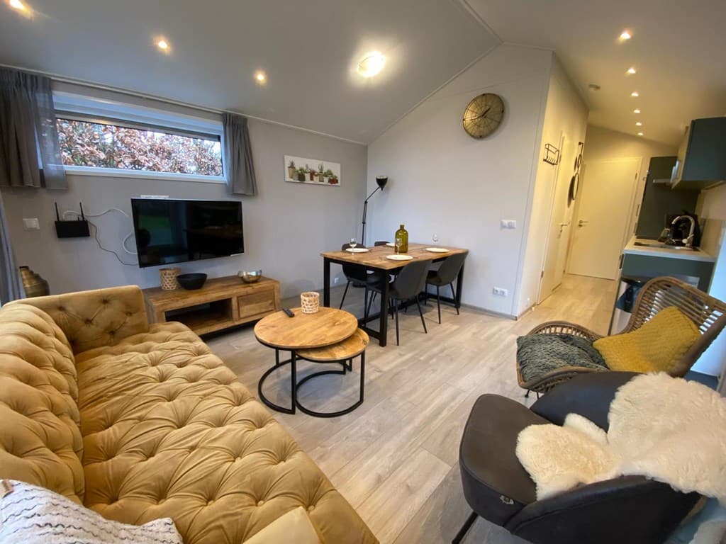 Woonkamer met een bank, eettafel, stoelen en televisie, lichte wanden en moderne inrichting