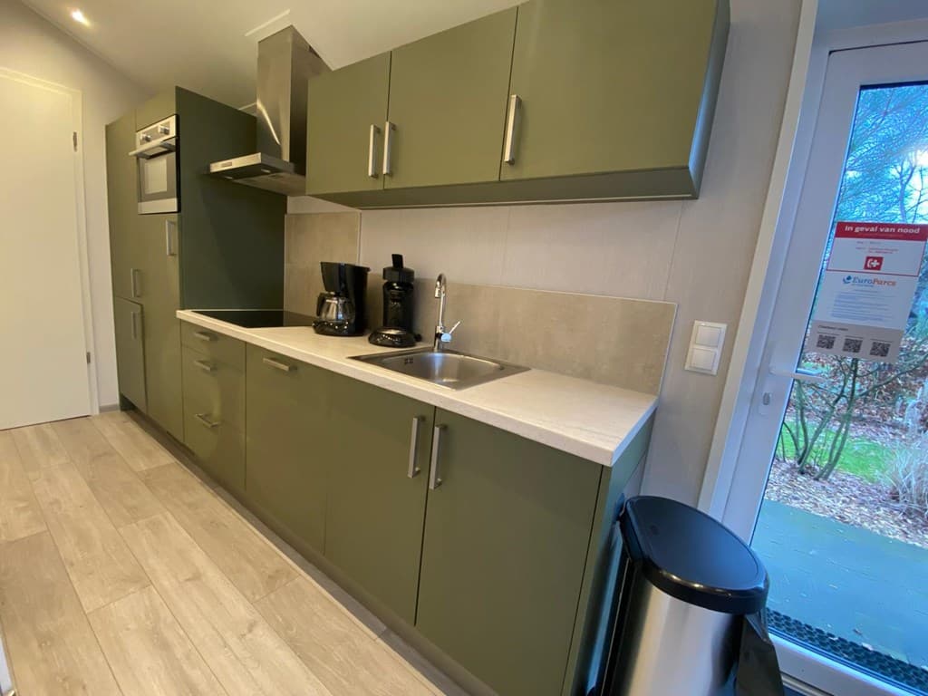 Keuken met groene keukenkastjes, een kookplaat, oven, spoelbak en koffiezetapparaten, lage kast en buitenzicht.