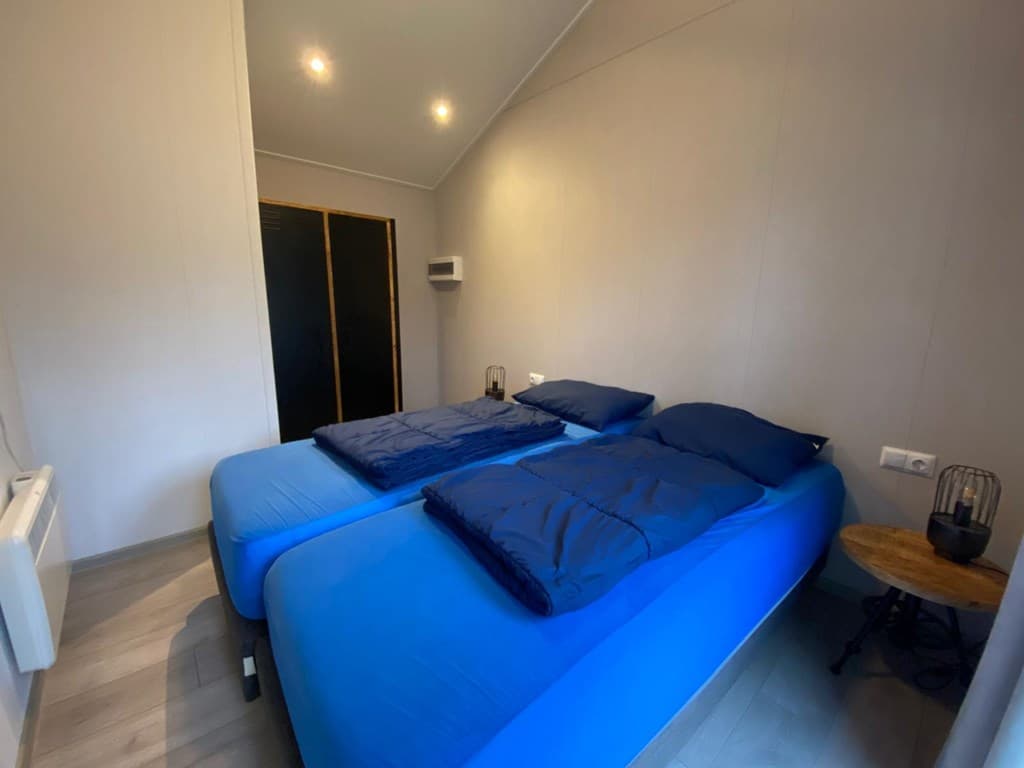 Slaapkamer met twee enkele bedden, blauwe dekbedden en een ronde tafel met lamp aan de muur.