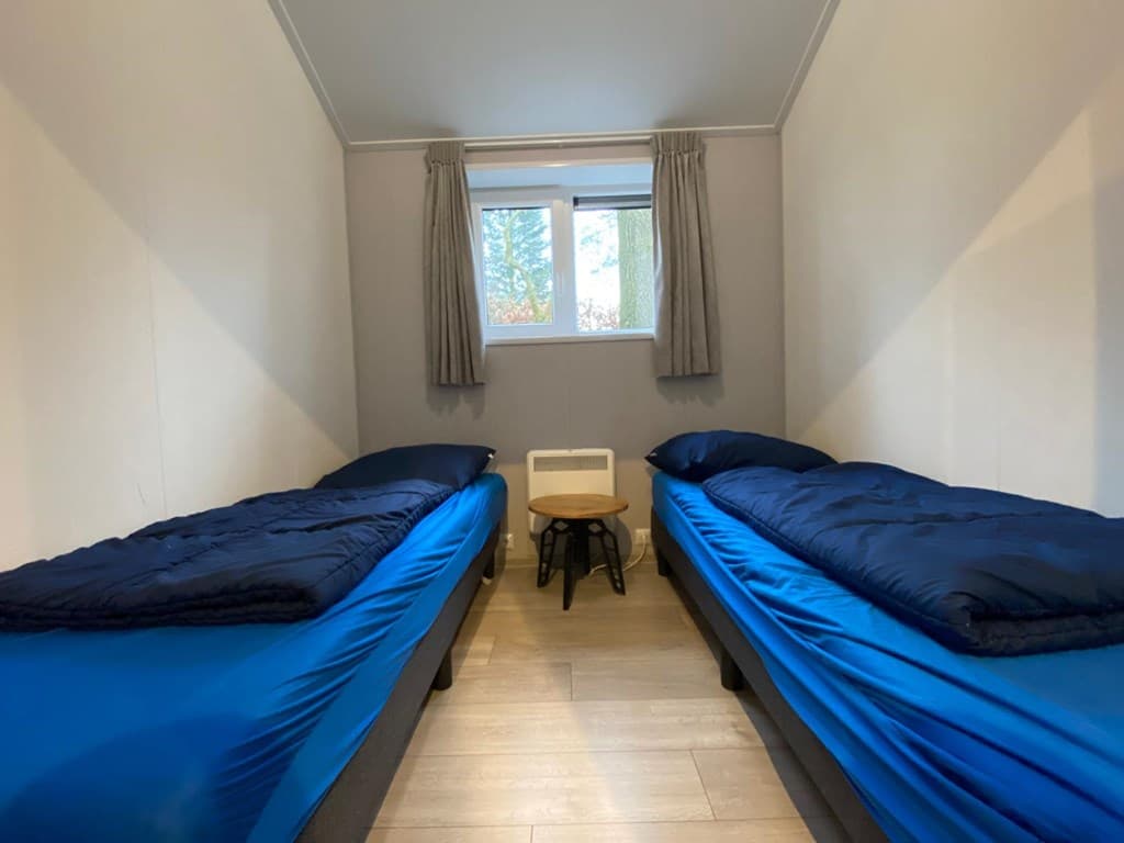 Slaapkamer met twee eenpersoonsbedden met blauwe dekbedden en een klein tafeltje tussen de bedden.