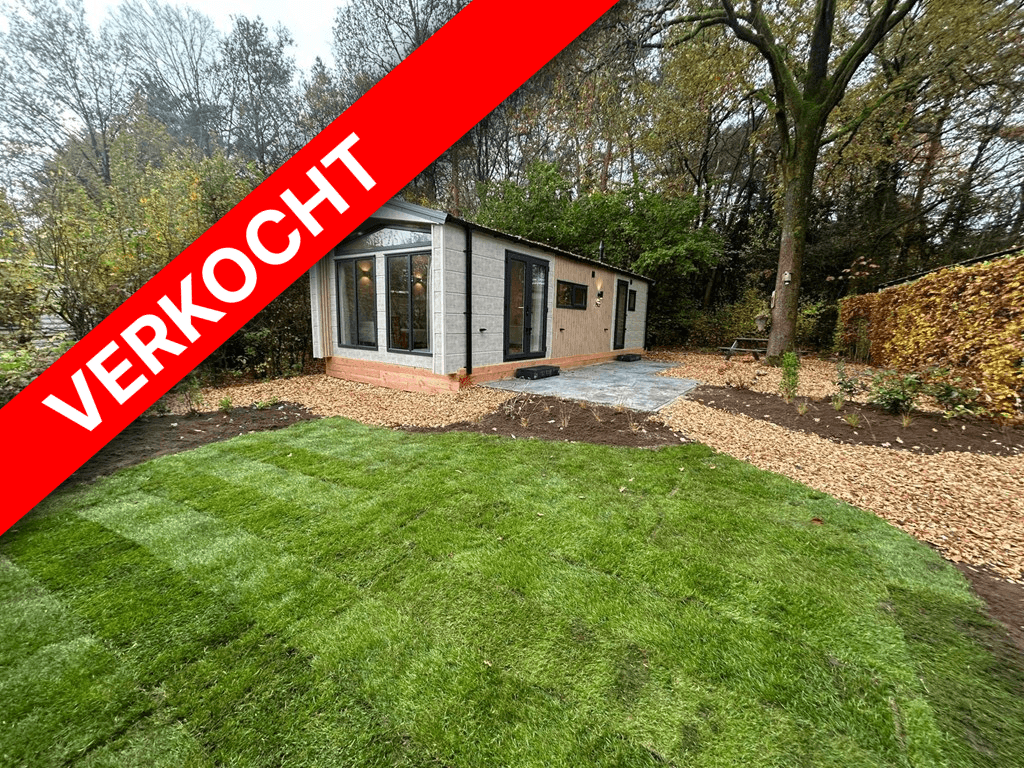 Moderne vakantiewoning omringd door bomen en groen gazon met terras en grindpad in Veluwepark de Bosgraaf.