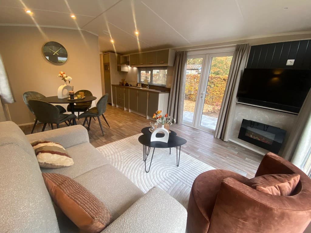 Woonkamer met bank, fauteuil, eettafel en open keuken met zicht op tuin en terrasdeuren.