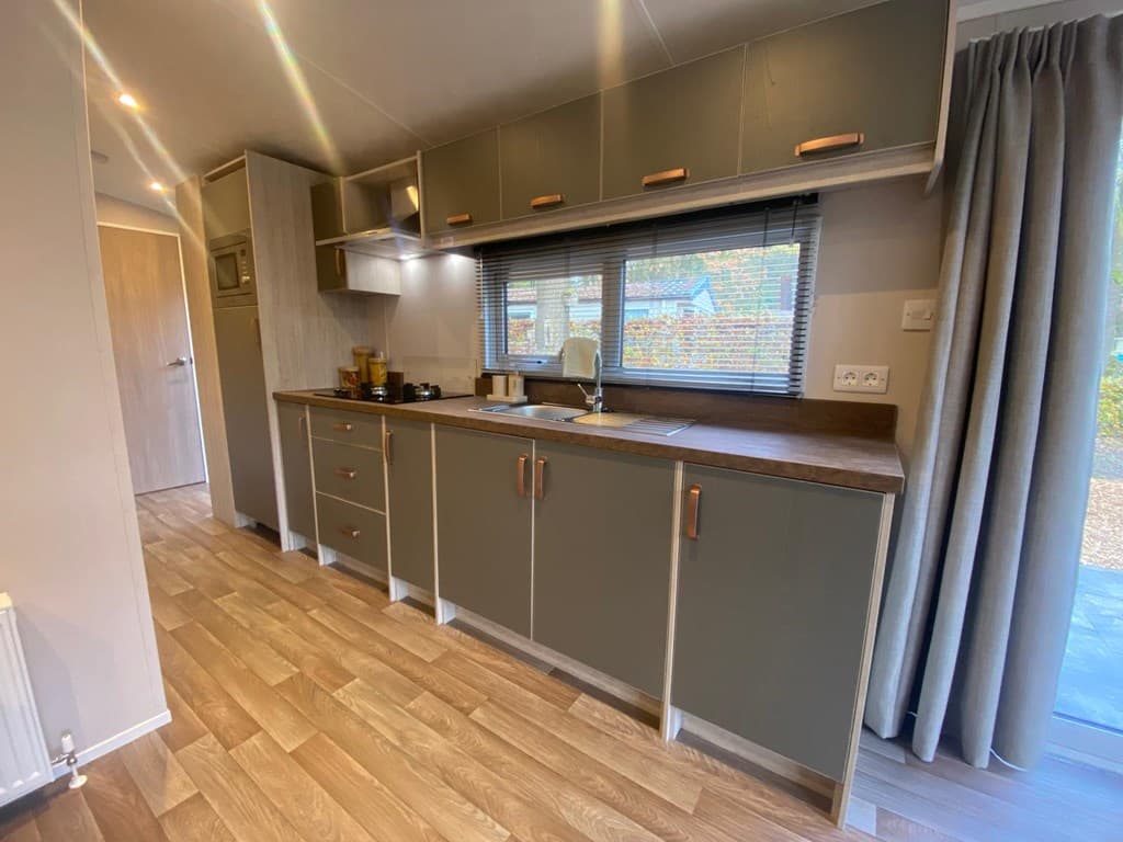 Moderne keuken met houten vloer, grijze kasten, venster en inbouwapparatuur.