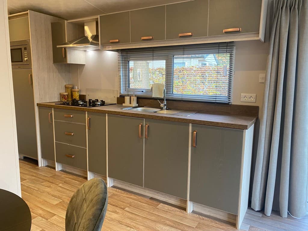 Moderne keuken met houten werkblad, gasfornuis en grote ramen met uitzicht op de buitenruimte.