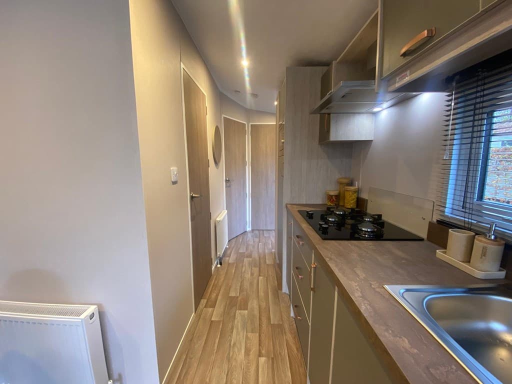 Keuken met moderne kastjes, aanrecht met spoelbak en gasfornuis, langs een smalle gang met deuren naar andere ruimtes.