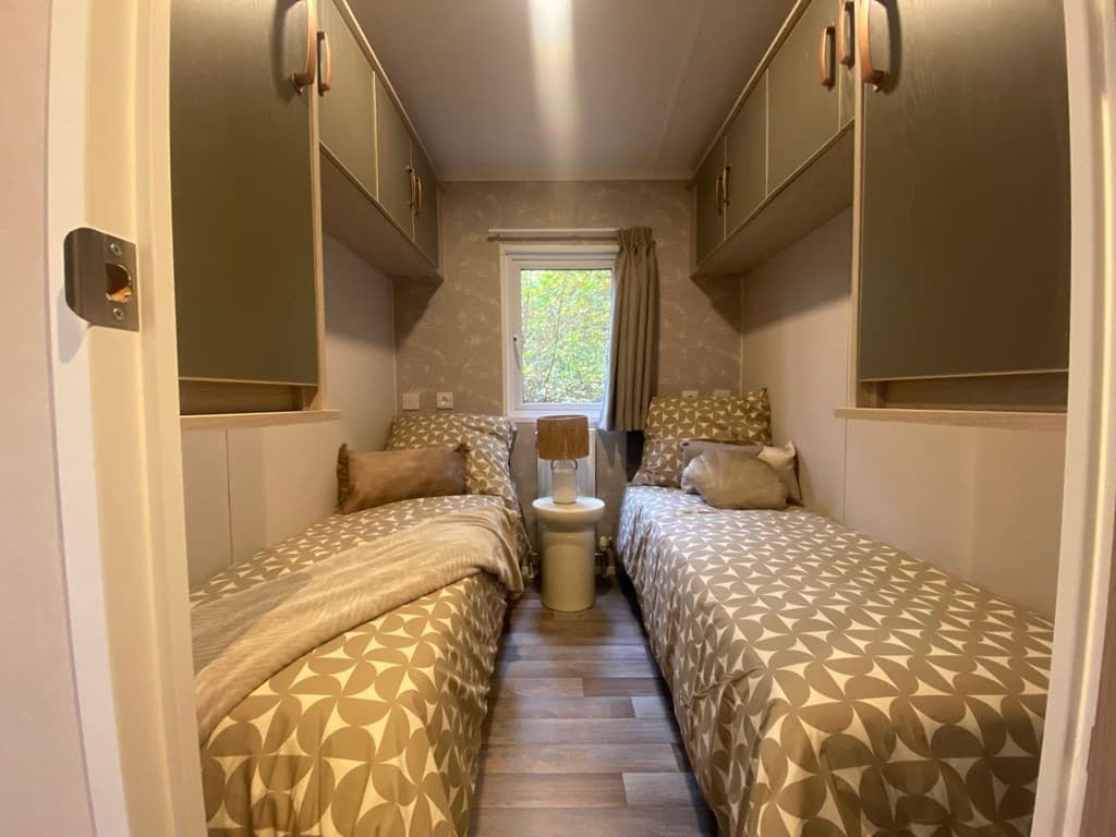 Slaapkamer met twee eenpersoonsbedden, moderne kasten en raam met uitzicht op groen park.