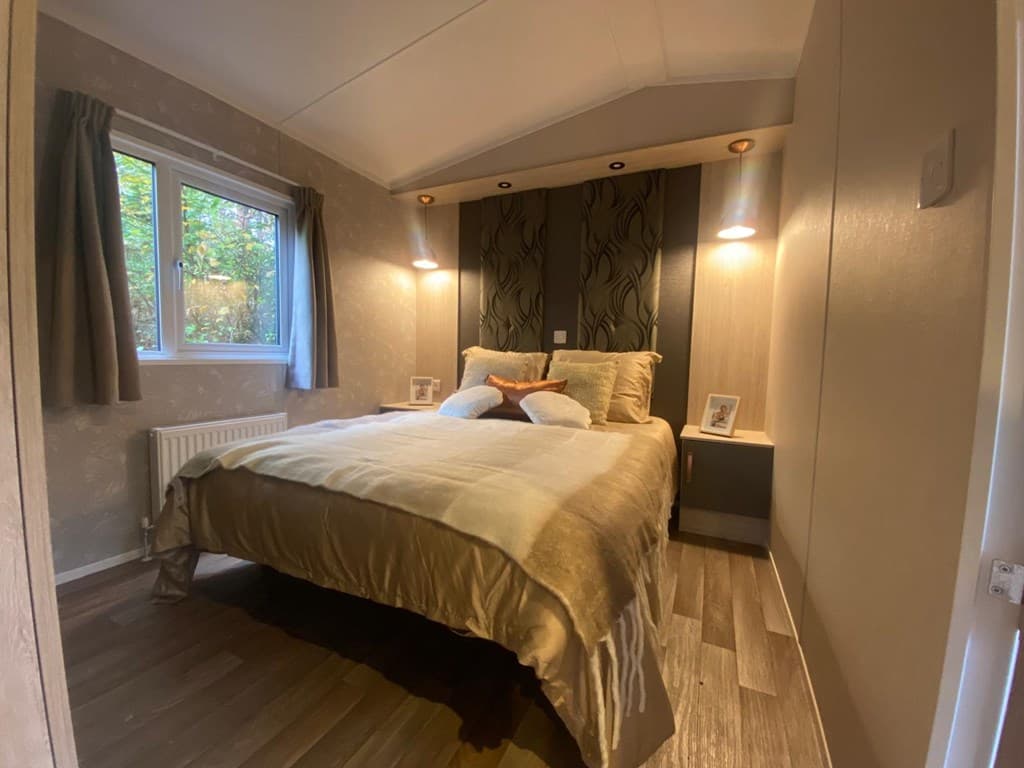Slaapkamer met een groot bed, sfeerverlichting, houten vloer en raam met uitzicht op de natuur.