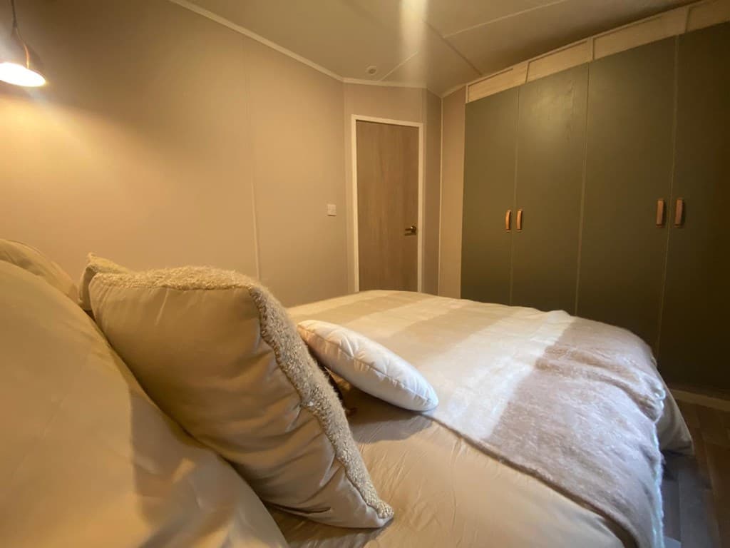 Slaapkamer met tweepersoonsbed, kussens en kast met groene deuren, rustige en nette uitstraling
