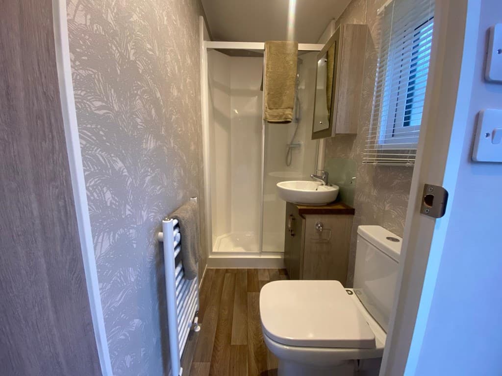 Badkamer met douchecabine, wastafel en toilet, lichtgrijze wanddecoratie en houten vloer.