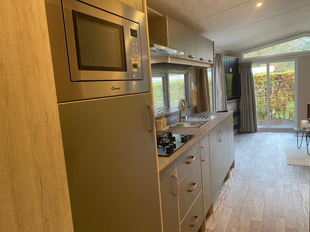 Keuken in een vakantiewoning met inbouwapparatuur, inclusief een magnetron en een kookplaat, met veel natuurlijk licht.