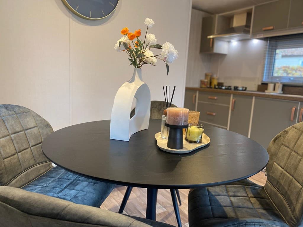 Eettafel met twee stoelen, bloemenvaas en decoratie in een moderne woonkamer met een keuken op de achtergrond
