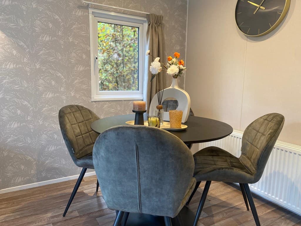 Eetkamer met een ronde zwarte tafel en vier stoffen stoelen, decoraties en een raam met uitzicht op de groene omgeving