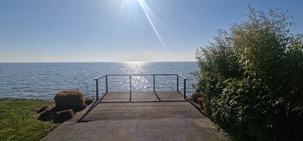 Uitzicht op het meer met een houten terras en een lichte begroeiing aan de zijkant onder een blauwe lucht