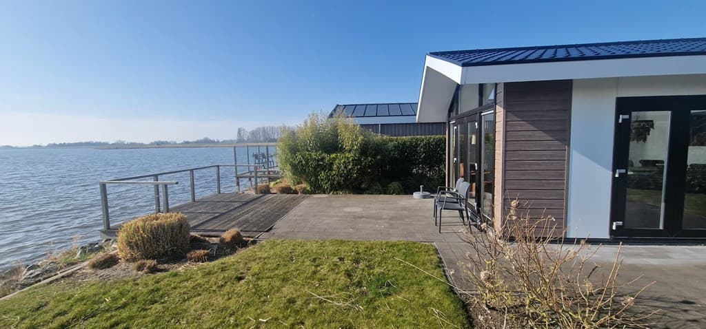 Moderne vakantiewoning aan het water met terras en uitzicht op het meer en omliggende begroeiing.