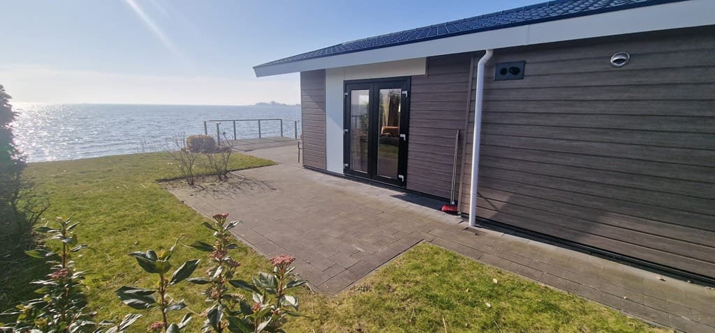 Moderne woning met otwonnende waterzicht, een betegeld terras en een verzorgde tuin met groene beplanting
