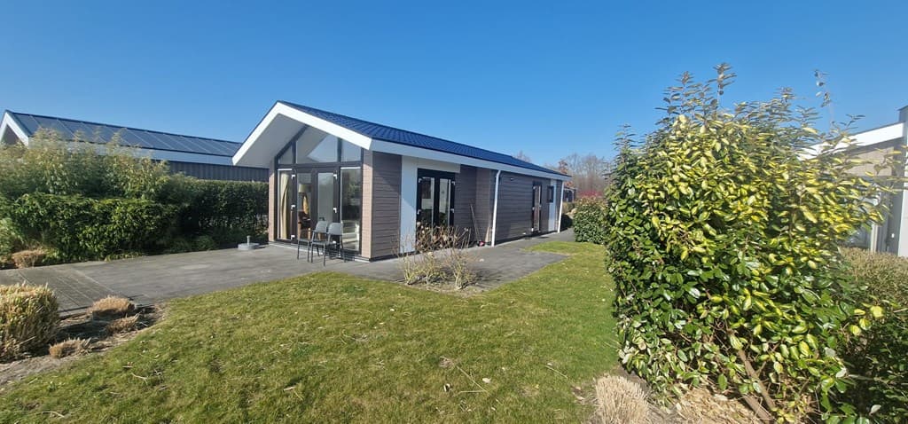 Moderne vakantiewoning met een tuin en een terras, omringd door groen en onder een heldere blauwe lucht.