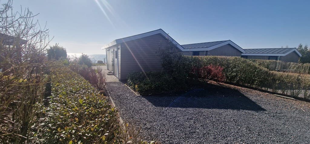 Vakantiehuis met omliggende groenvoorziening en gravelpad, uitzicht op water in de verte en andere woningen op de achtergrond
