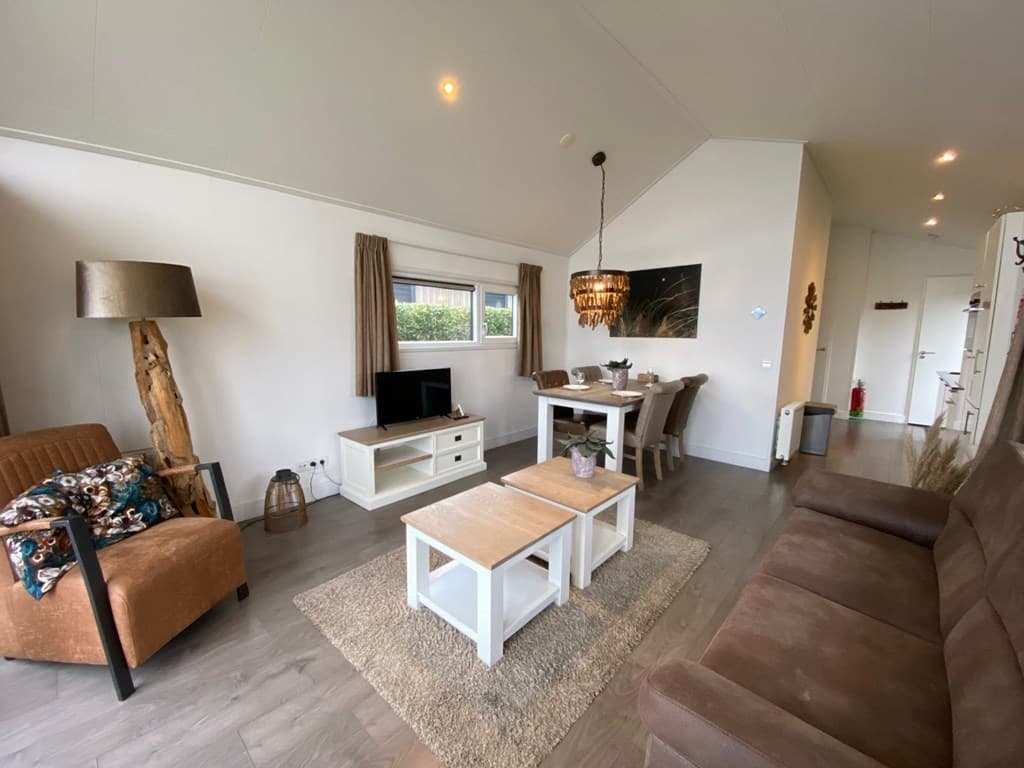 Woonkamer met bank, fauteuil, tv, eettafel en toegang naar buiten via een raam, lichte inrichting met moderne details