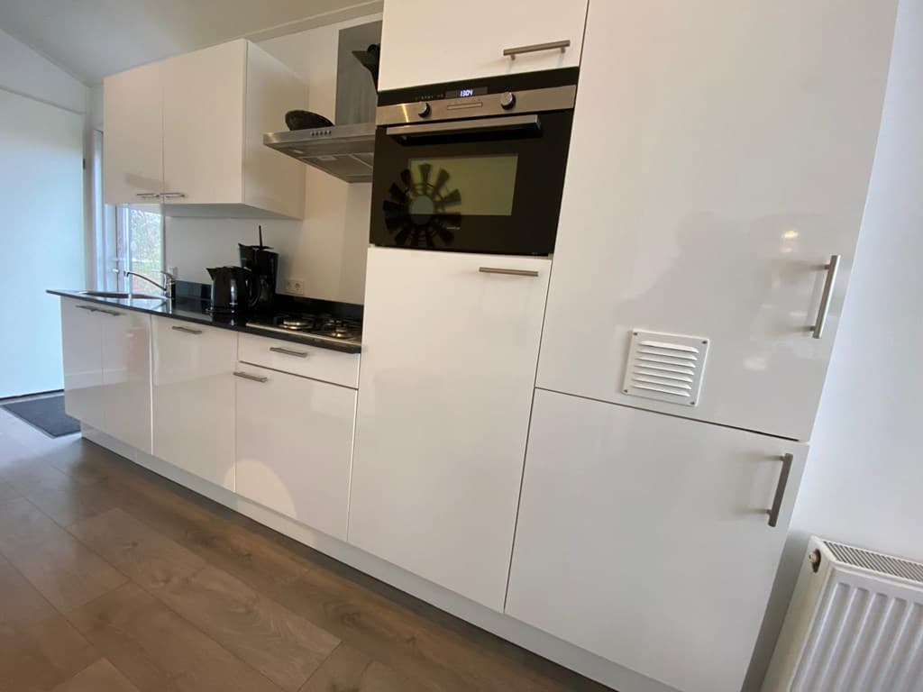 Witte keuken met moderne inbouwapparatuur, waaronder oven en kookplaat, en strakke kastjes op een houten vloer