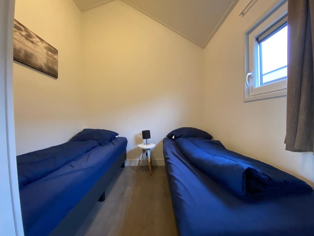 Slaapkamer met twee eenpersoonsbedden, een nachtkastje en een raam met gordijnen.