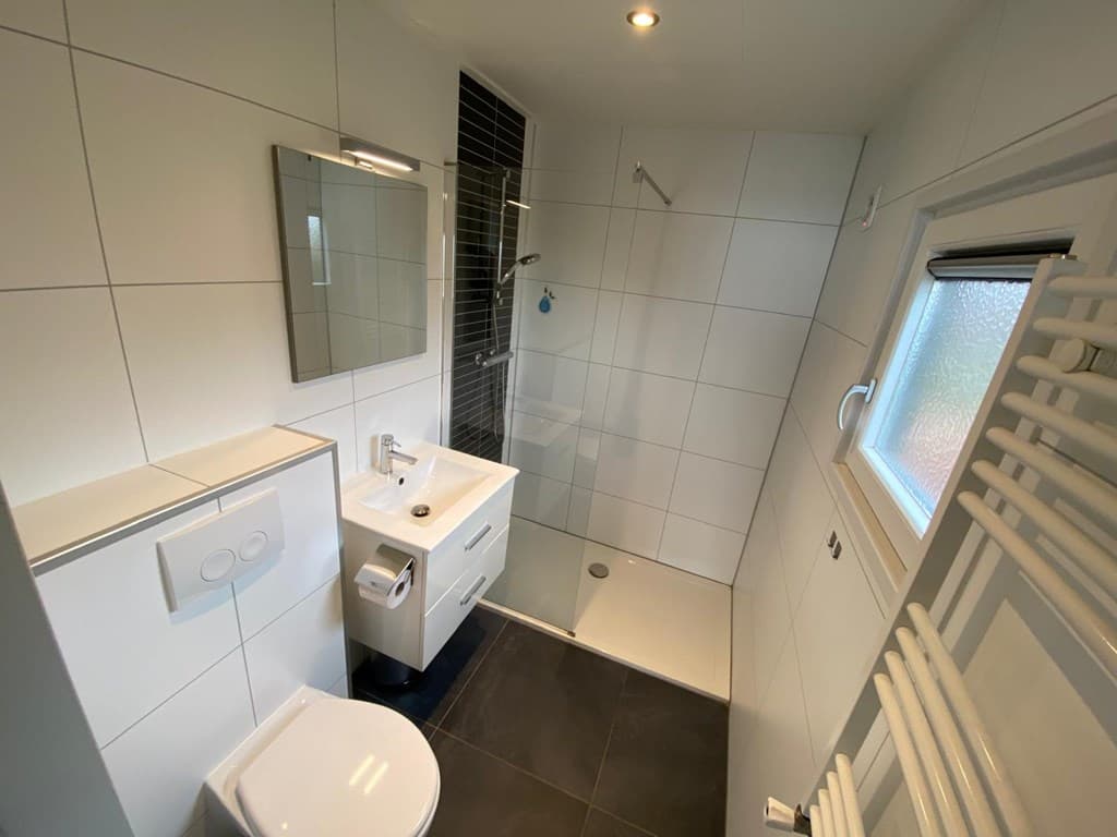 Moderne badkamer met inloopdouche, wastafel, toilet en handdoekenradiator in neutrale kleuren.