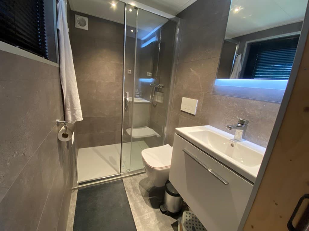 Moderne badkamer met douchecabine, wastafel en toilet, voorzien van grijze tegels en een groot raam voor natuurlijk licht